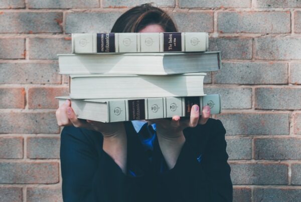 person holding pile of books near face